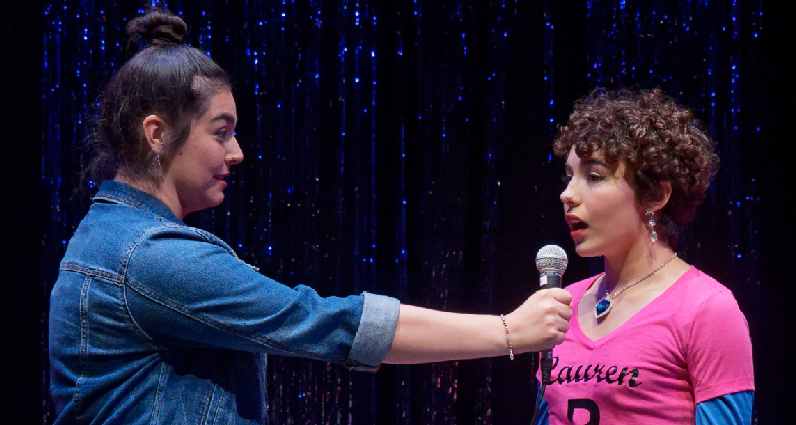 one woman holds a microphone up to another woman to speak into.